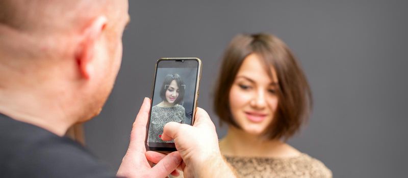 The hairdresser takes pictures of a woman finished short hairstyle on dark background