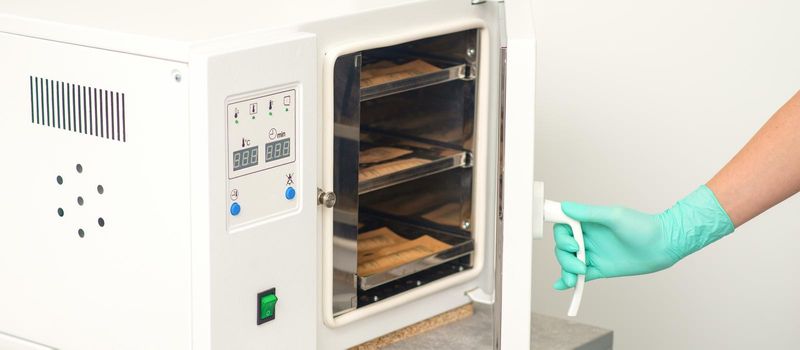 Beautician in protective gloves close the door of the machine for disinfection of tools before the depilation procedure