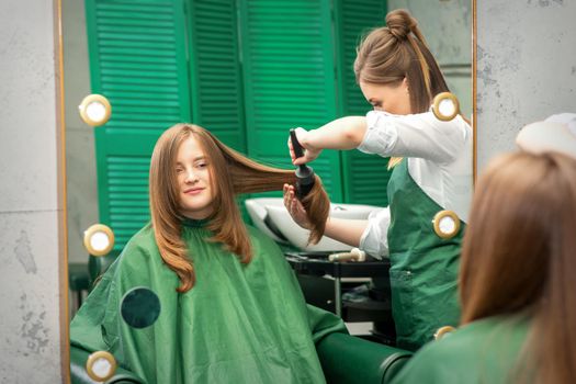 Hairdresser making hairstyling for the woman while combing with hairbrush, comb in a hair salon