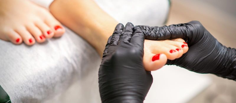 Foot massage with moisturizing and peeling cream by pedicurist hands wearing black gloves, close up