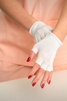 Cosmetician in workwear wearing white bamboo fingerless gloves on her hands in a beauty salon