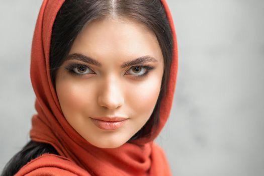 Portrait of a pretty young caucasian woman with makeup in a red headscarf on gray background