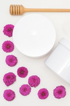 Flat lay composition of white jars with flowers on white background, skincare cosmetics, top view