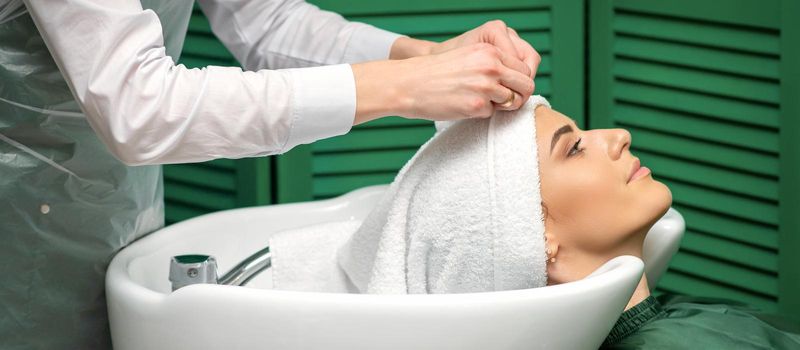 A hairdresser is wrapping a female head in a towel after washing hair in the beauty salon