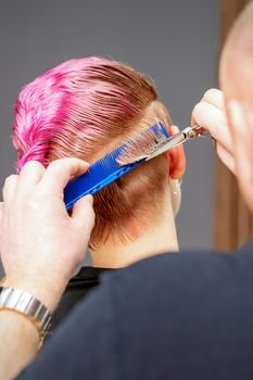 Woman having a new haircut. Male hairstylist cutting pink short hair with scissors in a hair salon