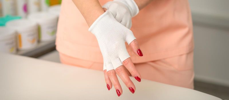 Cosmetician in workwear wearing white bamboo fingerless gloves on her hands in a beauty salon