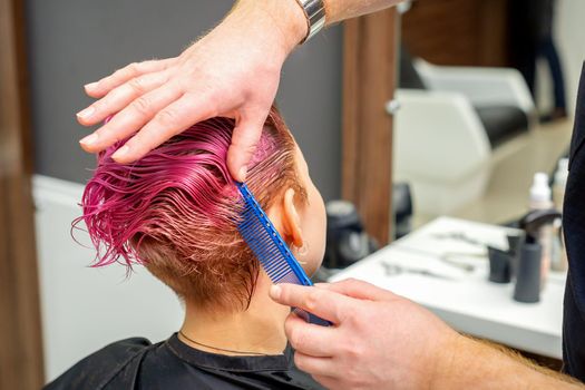 Hands of hairdresser combing hair making short pink hairstyle for a young caucasian woman in a beauty salon