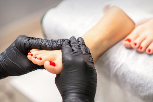 Foot massage with moisturizing and peeling cream by pedicurist hands wearing black gloves, close up