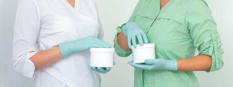 Two cosmeticians with jars of wax for depilation smiling against a white background. Natural product for hair removal. Copy space