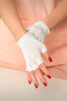 Cosmetician in workwear wearing white bamboo fingerless gloves on her hands in a beauty salon