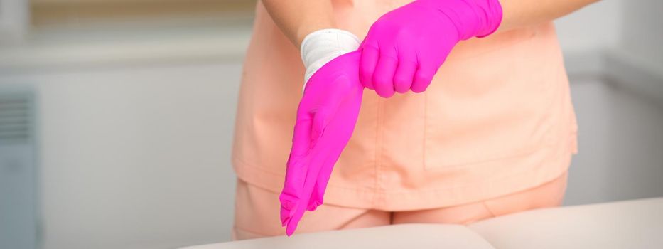 Hand of beautician puts on sterile pink gloves prepares to receive clients indoors