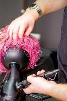Hair Stylist making hairstyle using hair dryer blowing on wet custom pink hair at a beauty salon