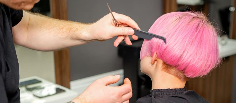 Hands of hairdresser combing hair making short pink hairstyle for a young caucasian woman in a beauty salon