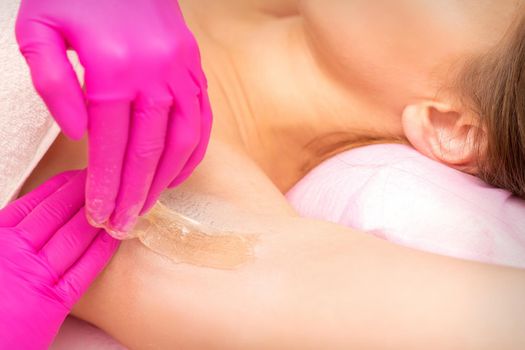 A beautician applies a sugar paste depilation under the female armpit in a beauty salon, close up