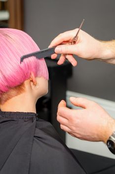 Hands of hairdresser combing hair making short pink hairstyle for a young caucasian woman in a beauty salon