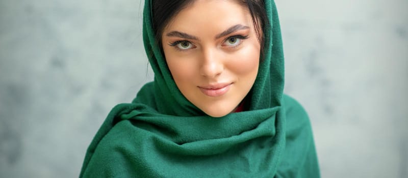 Portrait of a pretty young caucasian woman with makeup in a green headscarf on gray background