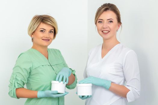 Two cosmeticians with jars of wax for depilation smiling against a white background. Natural product for hair removal. Copy space