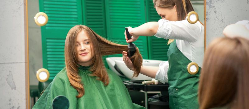 Hairdresser making hairstyling for the woman while combing with hairbrush, comb in a hair salon