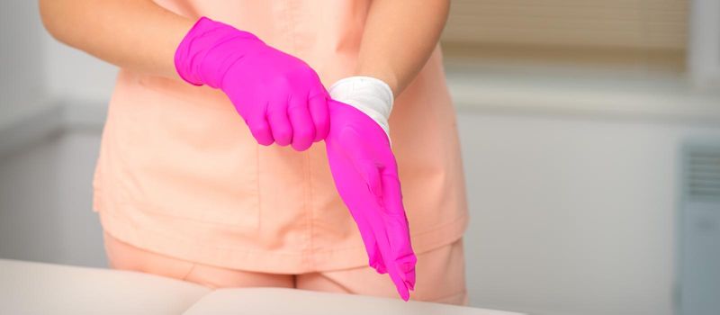 Hand of beautician puts on sterile pink gloves prepares to receive clients indoors