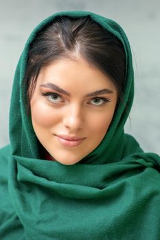 Portrait of a pretty young caucasian woman with makeup in a green headscarf on gray background