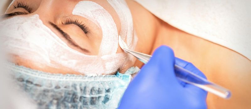 Face peeling at the beautician. Facial treatment. The beautician applies a cleansing face mask to the female patient