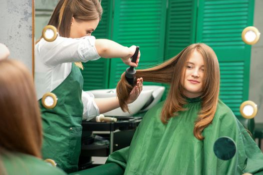 Hairdresser making hairstyling for the woman while combing with hairbrush, comb in a hair salon