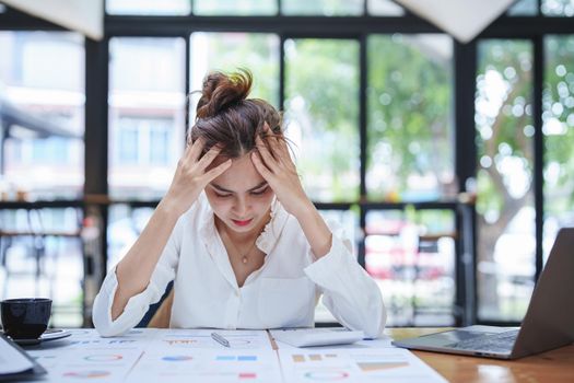 A portrait of a young employee showing an anxious and stressed face from working on paperwork on a desk.