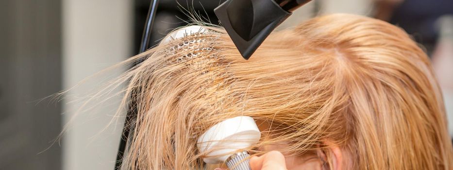 Hairdresser hand drying blond hair with a hairdryer and round brush in a beauty salon