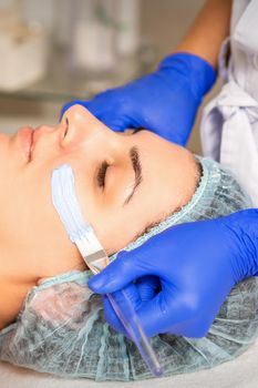 Face peeling at the beautician. Facial treatment. The beautician applies a cleansing face mask to the female patient