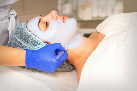 Face peeling at the beautician. Facial treatment. The beautician applies a cleansing face mask to the female patient