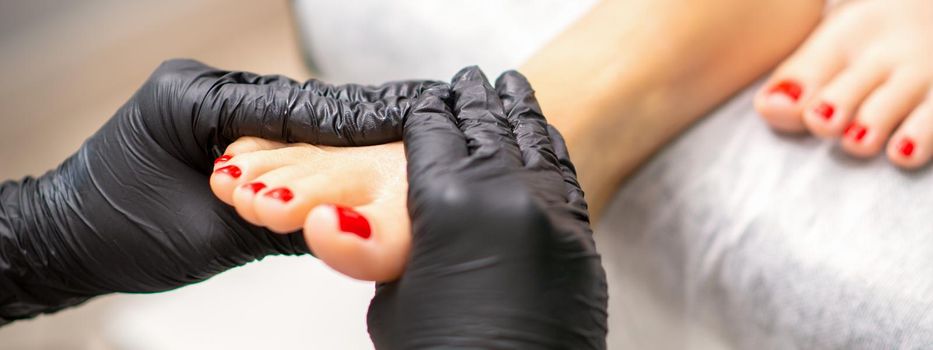 Foot massage with moisturizing and peeling cream by pedicurist hands wearing black gloves, close up