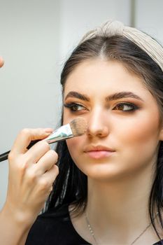 Closeup portrait of a woman applying dry cosmetic tonal foundation on the face using a makeup brush. Makeup detail