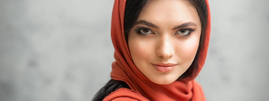 Portrait of a pretty young caucasian woman with makeup in a red headscarf on gray background