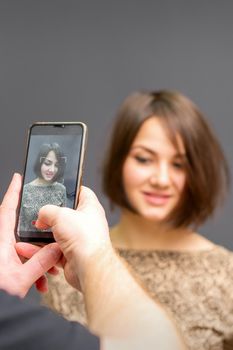 The hairdresser takes pictures of a woman finished short hairstyle on dark background