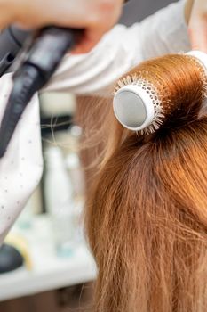 Drying red hair with a hairdryer and round brush, close up