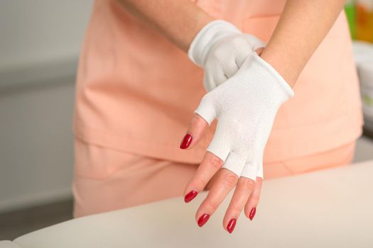 Cosmetician in workwear wearing white bamboo fingerless gloves on her hands in a beauty salon