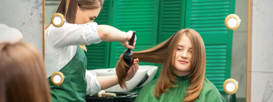 Hairdresser making hairstyling for the woman while combing with hairbrush, comb in a hair salon