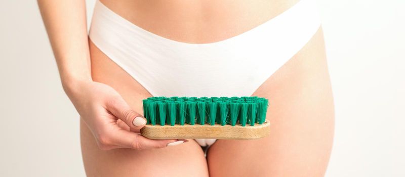 A woman in white panties holds a clothes brush on a white background. Depilation on the bikini zone