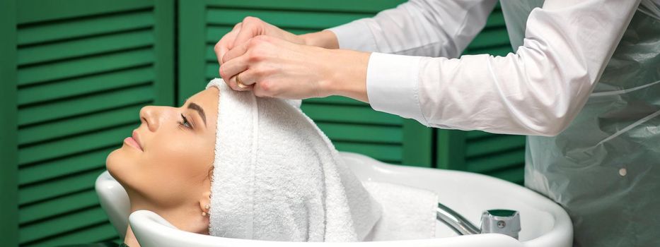 A hairdresser is wrapping a female head in a towel after washing hair in the beauty salon
