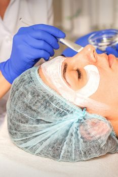 Face peeling at the beautician. Facial treatment. The beautician applies a cleansing face mask to the female patient