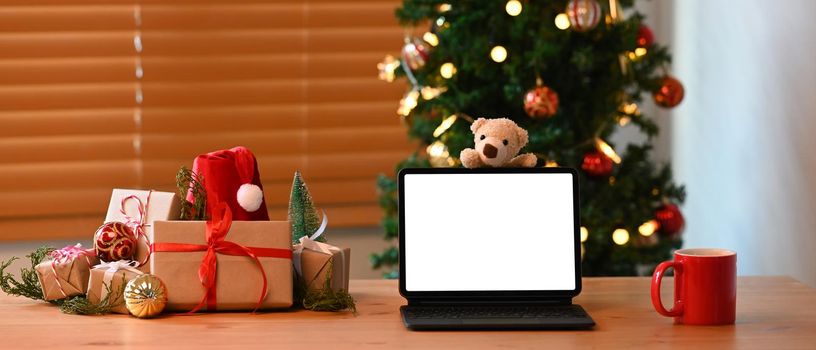 Computer tablet, cup of hot beverage and Christmas gift boxes on wooden table.