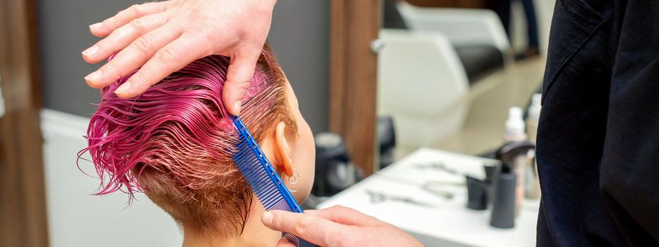 Hands of hairdresser combing hair making short pink hairstyle for a young caucasian woman in a beauty salon