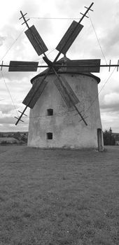 Black and white photo with an old windmill sitting in a field with a cloudy sky. High quality photo