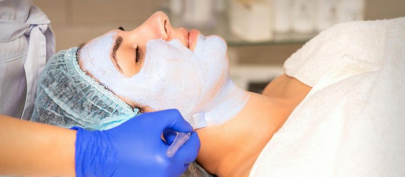 Face peeling at the beautician. Facial treatment. The beautician applies a cleansing face mask to the female patient