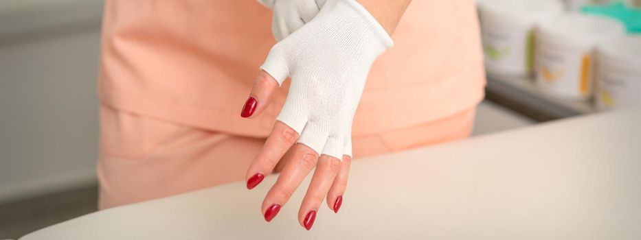 Cosmetician in workwear wearing white bamboo fingerless gloves on her hands in a beauty salon