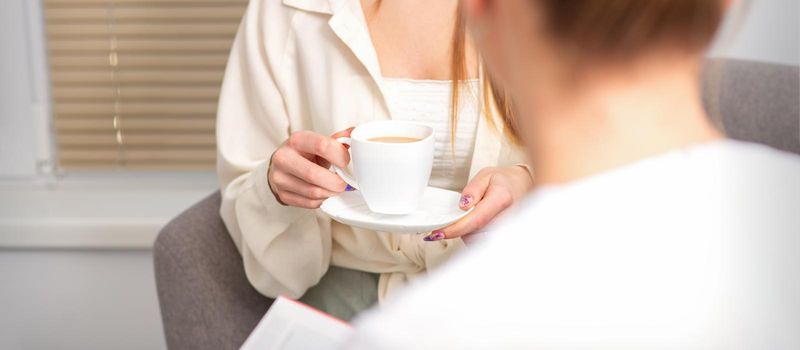 The young caucasian woman has a coffee and appointment with a female doctor in hospital office