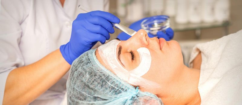 Face peeling at the beautician. Facial treatment. The beautician applies a cleansing face mask to the female patient