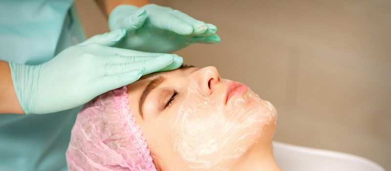 Face peeling at the beautician. Facial treatment. The beautician applies a cleansing face mask to the female patient