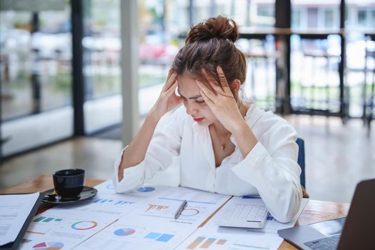 A portrait of a young employee showing an anxious and stressed face from working on paperwork on a desk.