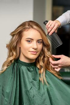 Hairdresser making hairstyling for the woman while combing with hairbrush, comb in a hair salon